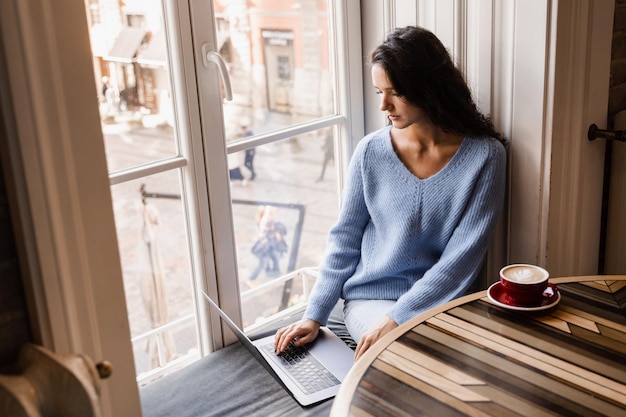 Aantrekkelijk meisje freelancer werkt online op laptop en drinkt koffie in café Zelfverzekerde zakenvrouw manager met laptop werkt online met collega's in café