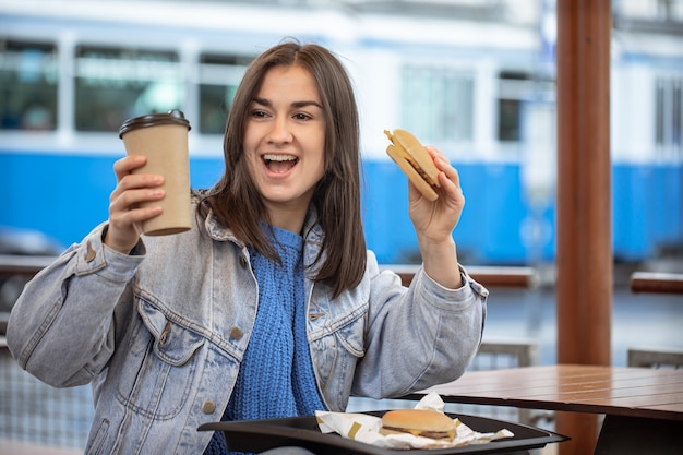 Aantrekkelijk meisje in casual stijl geniet van fastfood zittend op het zomerterras