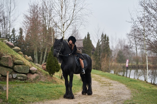 Foto aantrekkelijk meisje in een jurk rijden op een donker paard