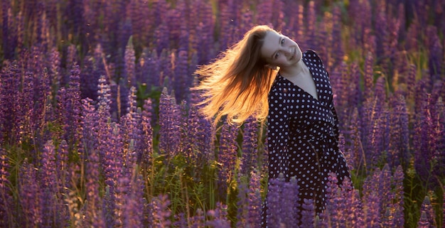 Aantrekkelijk meisje in een lange paarse jurk op een veld met lupine.