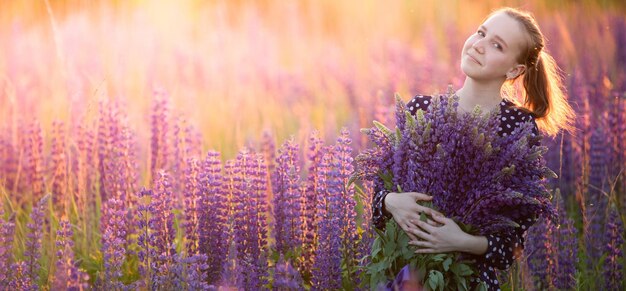 Aantrekkelijk meisje in een lange paarse jurk op een veld met lupine.