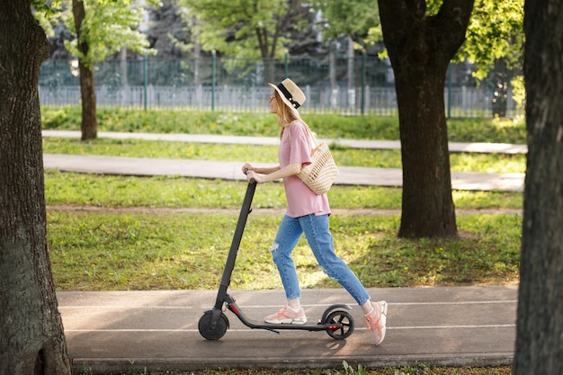 Aantrekkelijk meisje in strohoed met scooter in het park op een zomerse wandeling