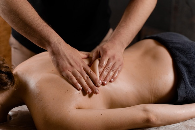 Aantrekkelijk meisje is ontspannen op klassieke massage procedure in spa. Manuele therapie. Masseur doet rugmassage.