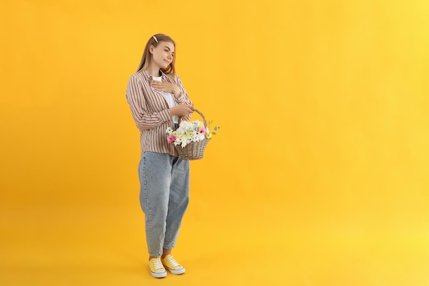 Aantrekkelijk meisje met mand met bloemen op gele achtergrond