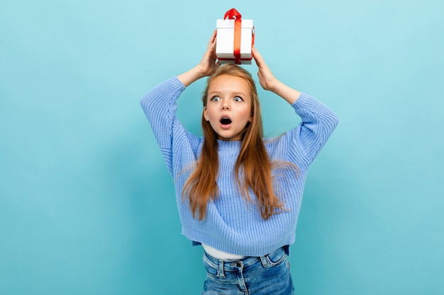 Aantrekkelijk meisje staat tegen een muur met een geschenk op haar hoofd met een rood lint