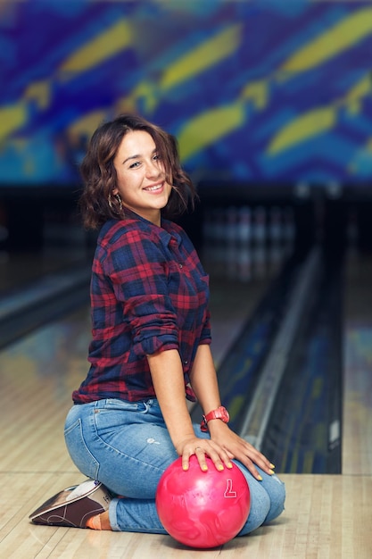 Aantrekkelijk meisje zittend met bal op de vloer in de bowlingclub