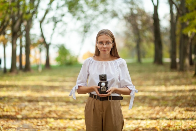 Foto aantrekkelijk mooi jong meisje met retro vintage dubbele lens reflectie camera in herfst park