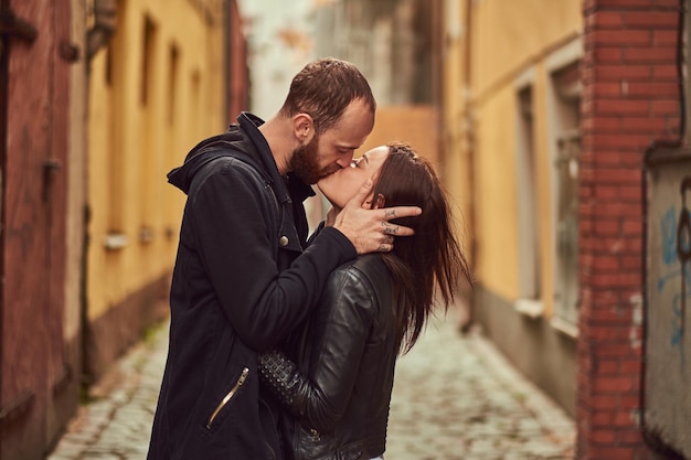Aantrekkelijk paar, bebaarde man en brunette meisje zoenen buiten oude Europese straat op een achtergrond.