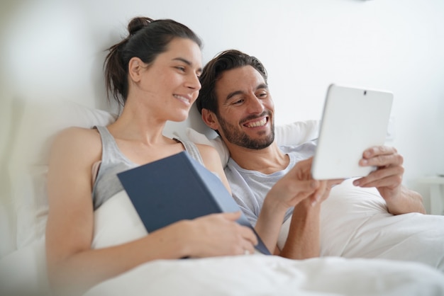 Aantrekkelijk paar lezen en ontspannen in bed met boek en tablet