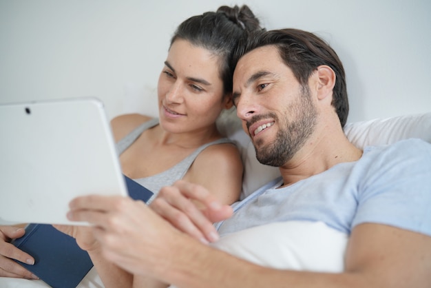 Aantrekkelijk paar lezen en ontspannen in bed met boek en tablet