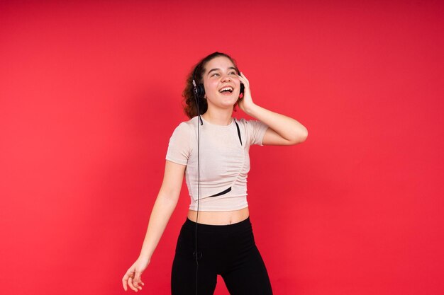 Aantrekkelijk sportfitness tienermeisje met koptelefoon op rode achtergrond