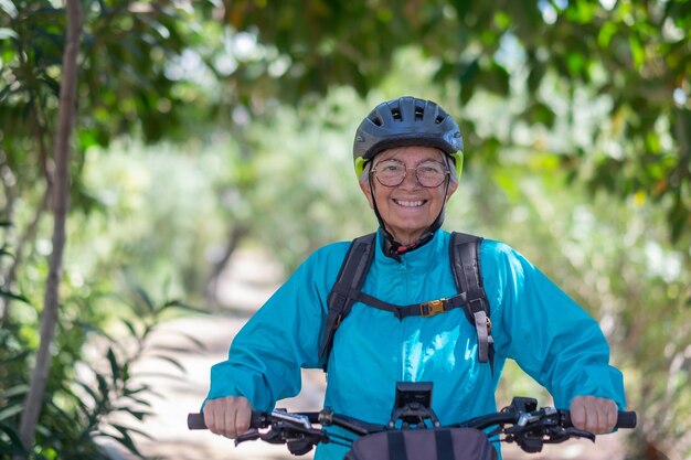 Aantrekkelijke actieve senior vrouw met electrobike die buiten in het park staat Gelukkige oudere vrouw die in de natuur loopt met haar fiets die geniet van vrijheid en een gezonde levensstijl