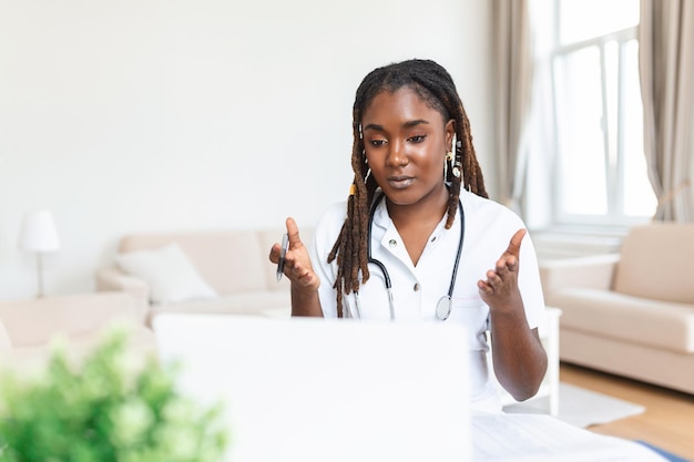 Aantrekkelijke Afrikaanse vrouwelijke arts die praat terwijl hij de medische behandeling aan de patiënt uitlegt via een videogesprek met laptop in het consult