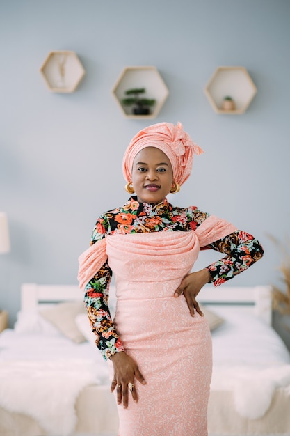 Aantrekkelijke Afro-Amerikaanse modevrouw in roze kleurrijke traditionele kleding en hoofddoek in moderne studio