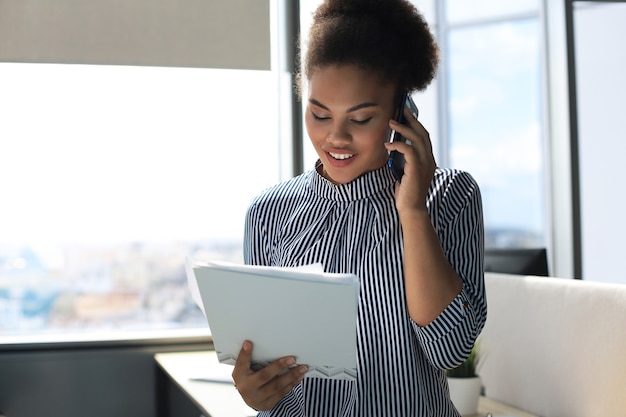 Aantrekkelijke Afro-Amerikaanse zakenvrouw praten met collega's op de mobiele telefoon.