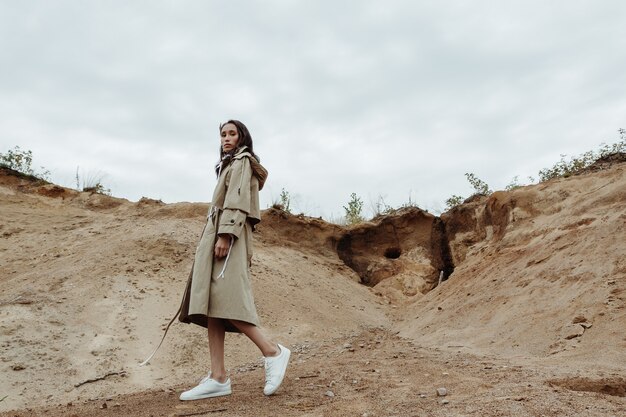 Aantrekkelijke Aziatische jonge vrouw lopen door de zandgroeve in een beige stijlvolle trenchcoat in de herfst.