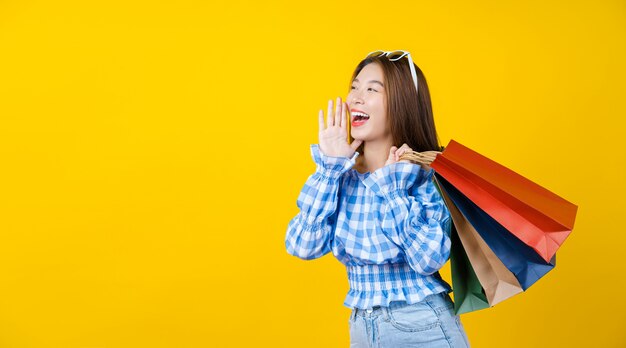 Aantrekkelijke Aziatische lachende jonge vrouw met winkelen coloful tas op aisolated gele muur