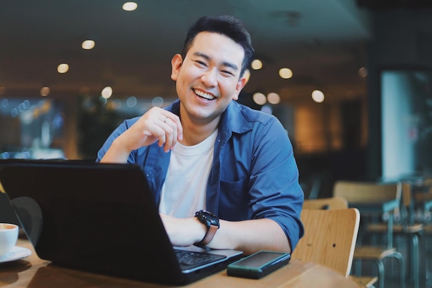 Aantrekkelijke Aziatische man in blauw shirt aan het werk in café Glimlachende Aziatische man die koffie drinkt