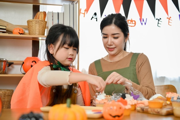 Aantrekkelijke Aziatische moeder die haar dochter helpt een Halloween-cupcake te versieren voor hun feest