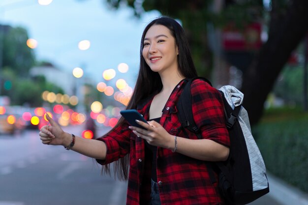 Aantrekkelijke Aziatische solo-reiziger die lokaal taxivervoer belt met smartphone en rugzak