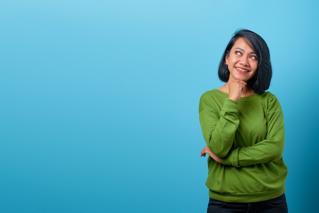 Aantrekkelijke Aziatische vrouw die kin aanraakt met een glimlachuitdrukking op blauwe achtergrond