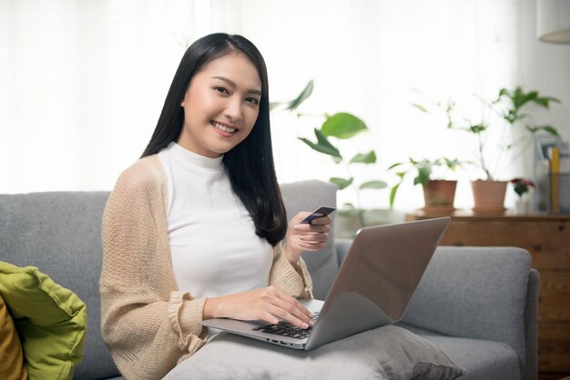 Aantrekkelijke aziatische vrouw die online winkelt gebruik smartphone-laptop en creditcard voor betaling