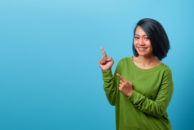 Aantrekkelijke Aziatische vrouw die vrijetijdskleding draagt, lacht en wijst met twee handen naar de zijkant