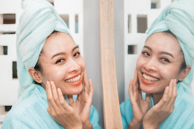 Aantrekkelijke Aziatische vrouw die zich voor spiegel met handdoek bevindt bij de badkamers