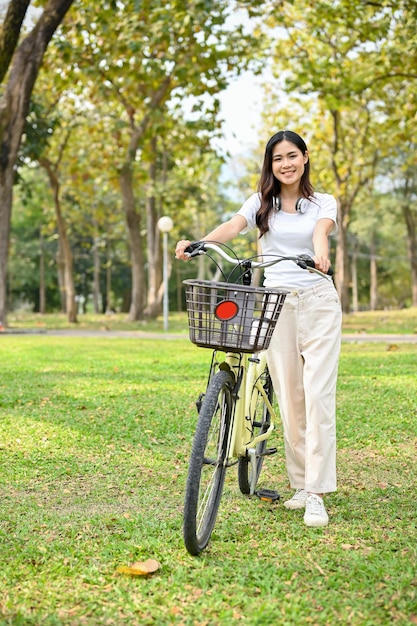 Aantrekkelijke Aziatische vrouw in vrijetijdskleding die met een fiets in het openbare park loopt