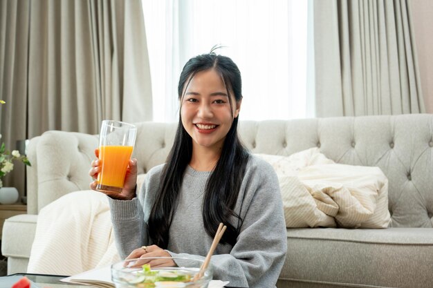 Aantrekkelijke Aziatische vrouw lacht met een glas sinaasappelsap in haar hand terwijl ze aan een koffietafel zit