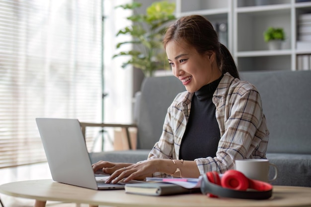 Aantrekkelijke Aziatische vrouwelijke freelancer die haar project plant en aan haar taken werkt op een laptop op een koffietafel in haar woonkamer