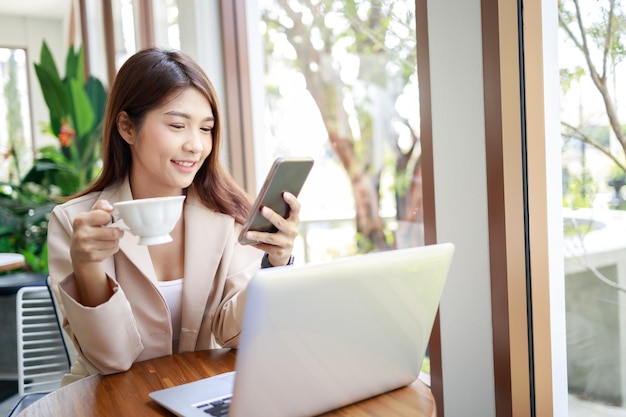 Aantrekkelijke aziatische zakenvrouw die smartphone gebruikt en met een laptop in de coffeeshop werkt