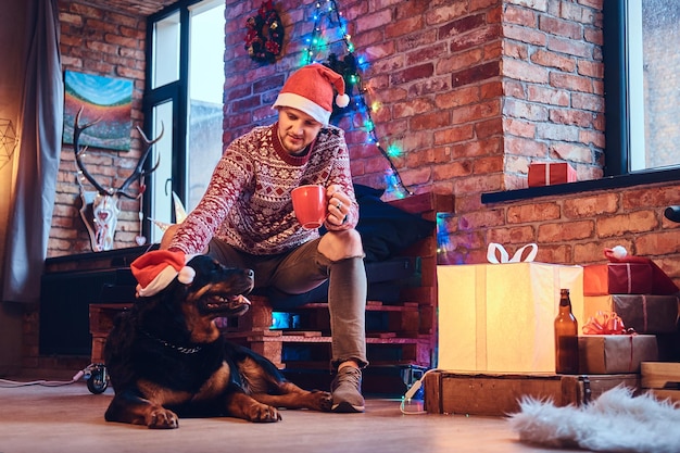 Aantrekkelijke bebaarde hipster man met zijn Rottweiler hond in een kamer met kerstversiering.