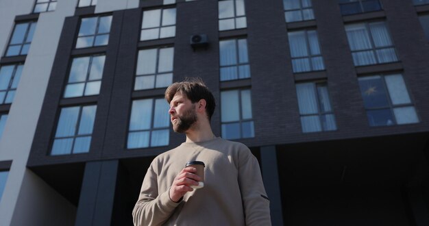 Aantrekkelijke bebaarde man met afhaalbeker met koffiekantoorcentrum op de achtergrond