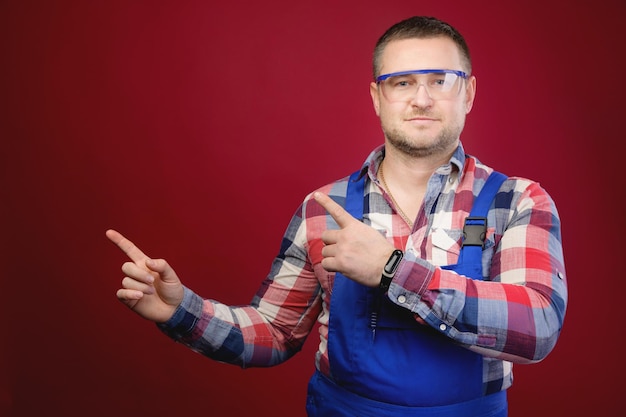 Foto aantrekkelijke blanke mannelijke voorman in uniform en bril wijst met de vinger naar lege ruimte voorman