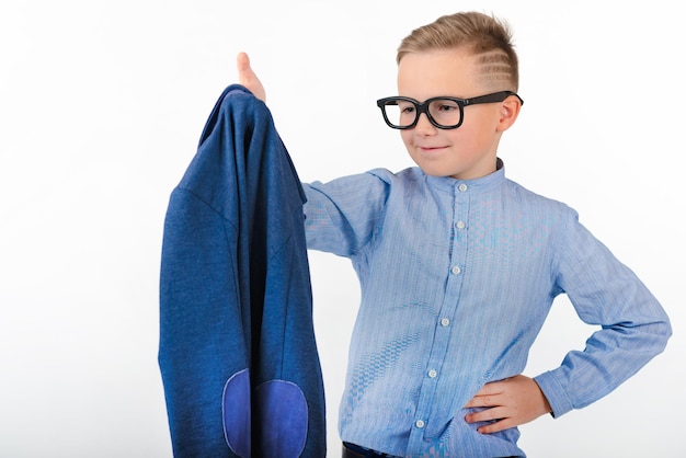 Aantrekkelijke blanke schooljongen met een bril en een blauw shirt kijkt rechtstreeks in zijn blauwe jas.