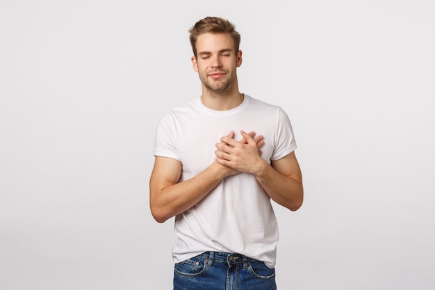Aantrekkelijke blonde bebaarde man in wit T-shirt met handen op het hart