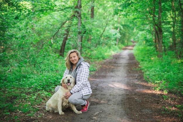 aantrekkelijke blonde die een hond knuffelt op het pad in het bos