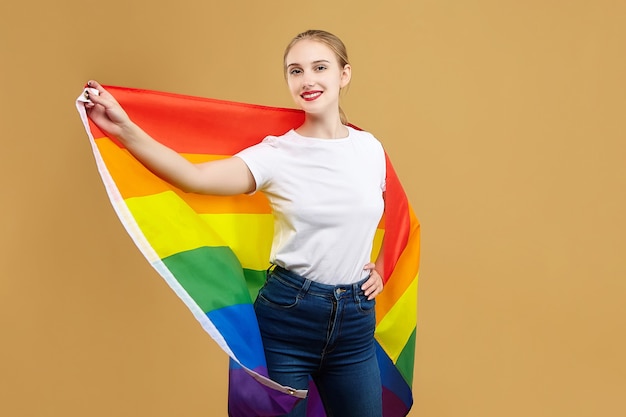 Aantrekkelijke blonde maakte poseren met een regenboog Lgbt-vlag. fotoshoot in de studio op een gele achtergrond.