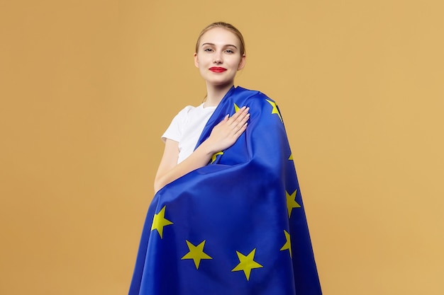 Foto aantrekkelijke blonde poseert met de vlag van de europese unie. fotoshoot in de studio op een gele achtergrond.