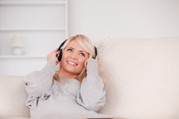 Aantrekkelijke blonde vrouw met hoofdtelefoons die in een bank liggen