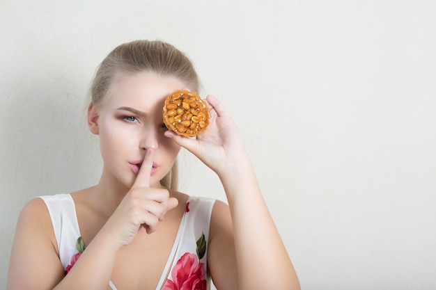 Aantrekkelijke blondevrouw die oog behandelt met cupcake, die stiltegebaar toont. ruimte voor tekst