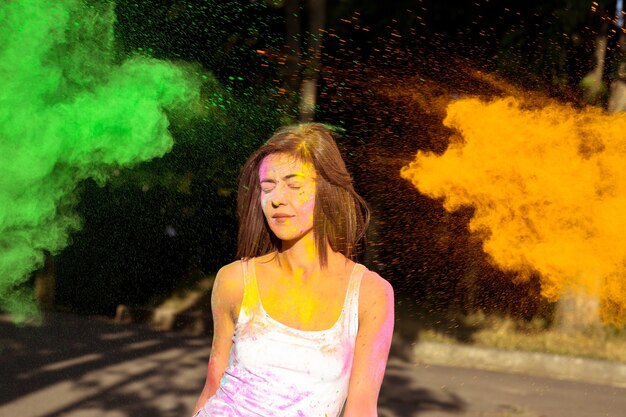 Aantrekkelijke brunette vrouw met kort haar poseren met exploderende groene en oranje Holi-verf