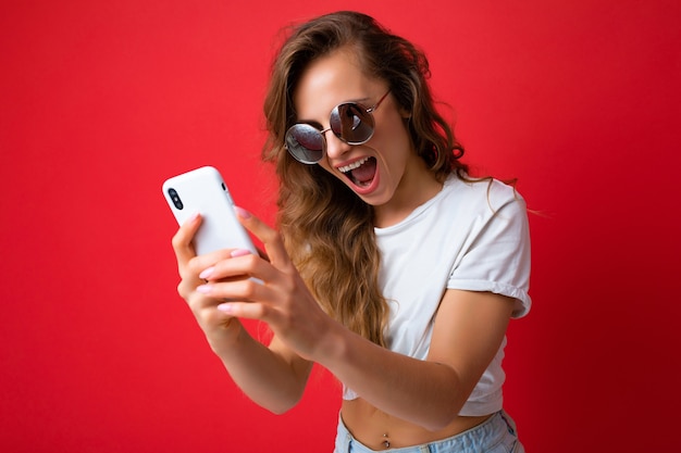 Aantrekkelijke charmante jonge lachende gelukkige vrouw houden en met behulp van mobiele telefoon nemen selfie stijlvolle kleding dragen