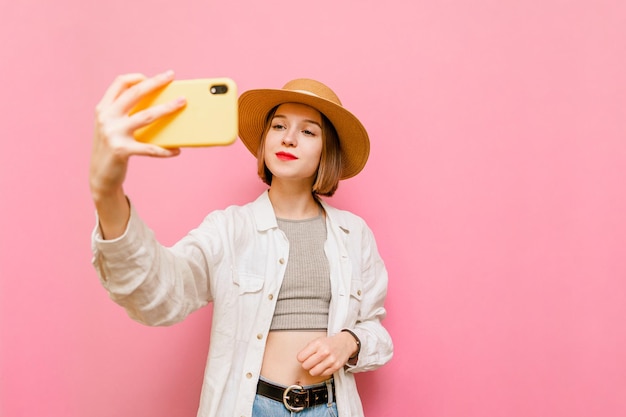 Aantrekkelijke dame in hoed en lichte kleding neemt selfie op smartphone geïsoleerd