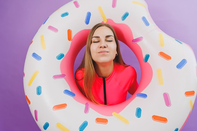 Aantrekkelijke emotionele vrouw in stijlvol roze zwempak met donut opblaasbare ring op effen achtergrond Strandmode