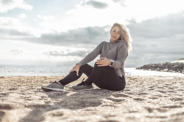 Aantrekkelijke fit sportvrouw zittend op het zand op een zonnige dag