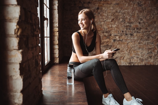 Aantrekkelijke fitness vrouw zitten in de sportschool luisteren muziek