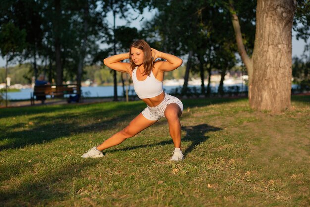 Aantrekkelijke fitnessvrouw met atletisch figuur die pilates doet en zich uitstrekt in het park