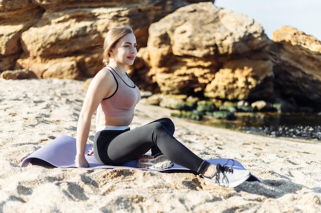 Aantrekkelijke fitnessvrouw zit op een mat op het strand Gezonde levensstijl